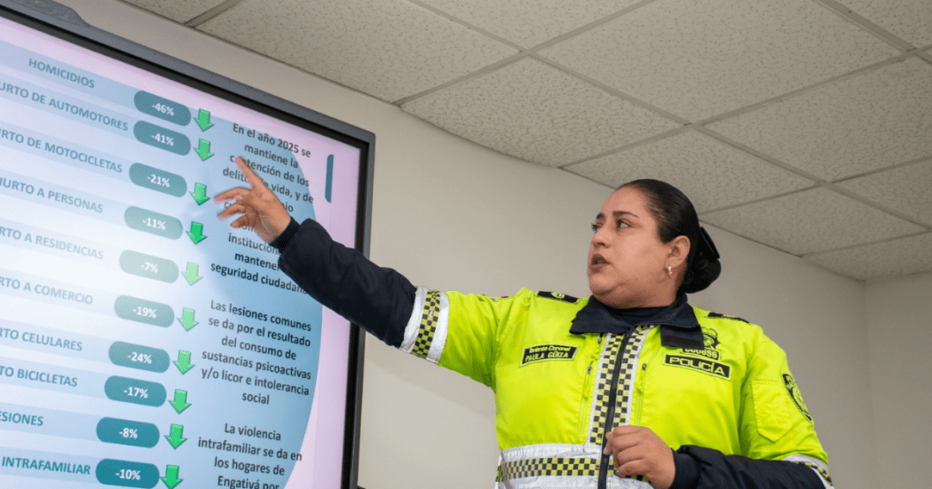Foto de una uniformada que presenta la reducción de delitos señalando las cifras en una pantalla.