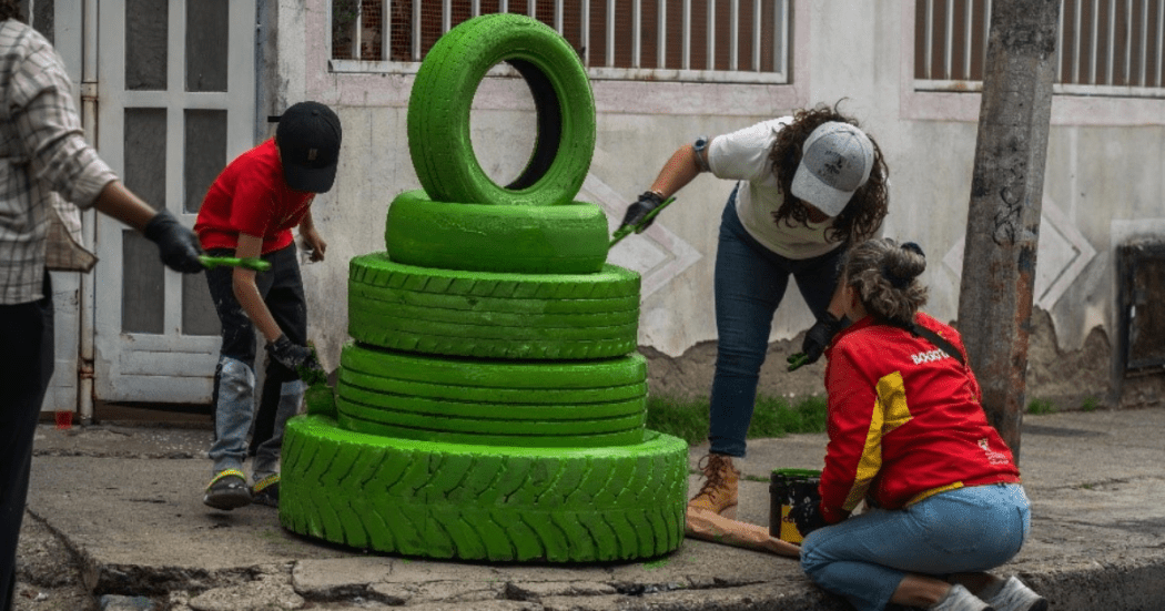Imagen de varias personas pintando de color verde unas llantas