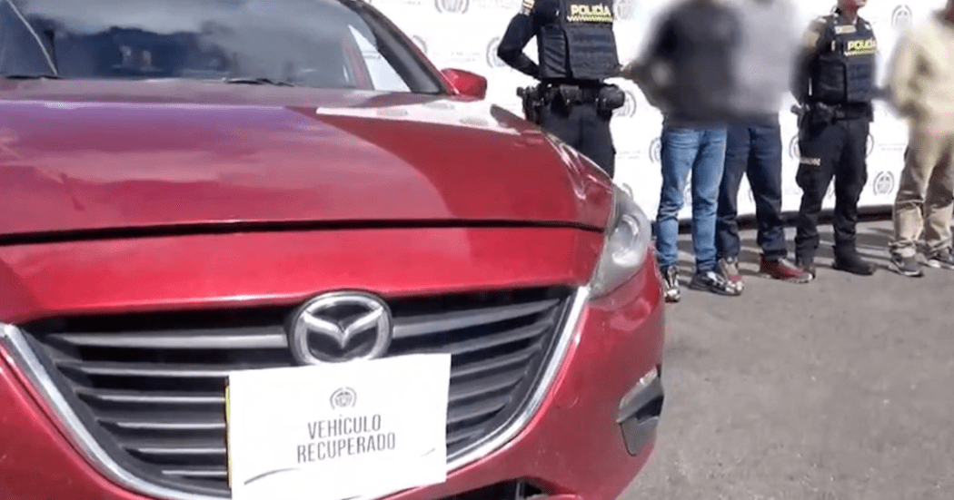 Imagen de un vehículo rojo y al lado hombres y agente de Policía de pie.