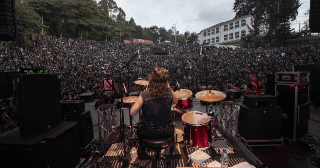 Imagen de una banda de rock en el escenario, de frente se encuentran muchas personas en el público
