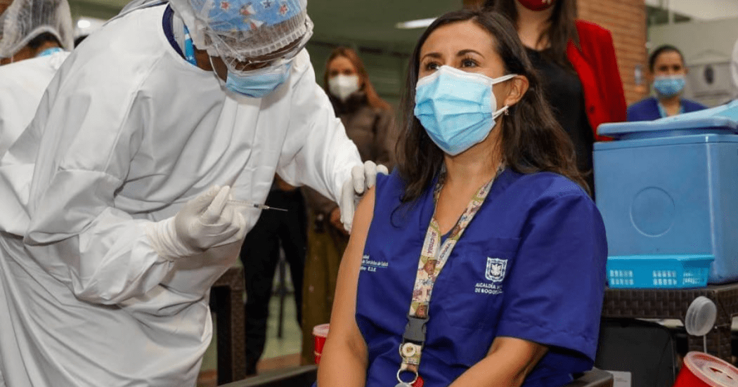 Imagen de mujer sentada y junto a ella una enfermera la vacuna