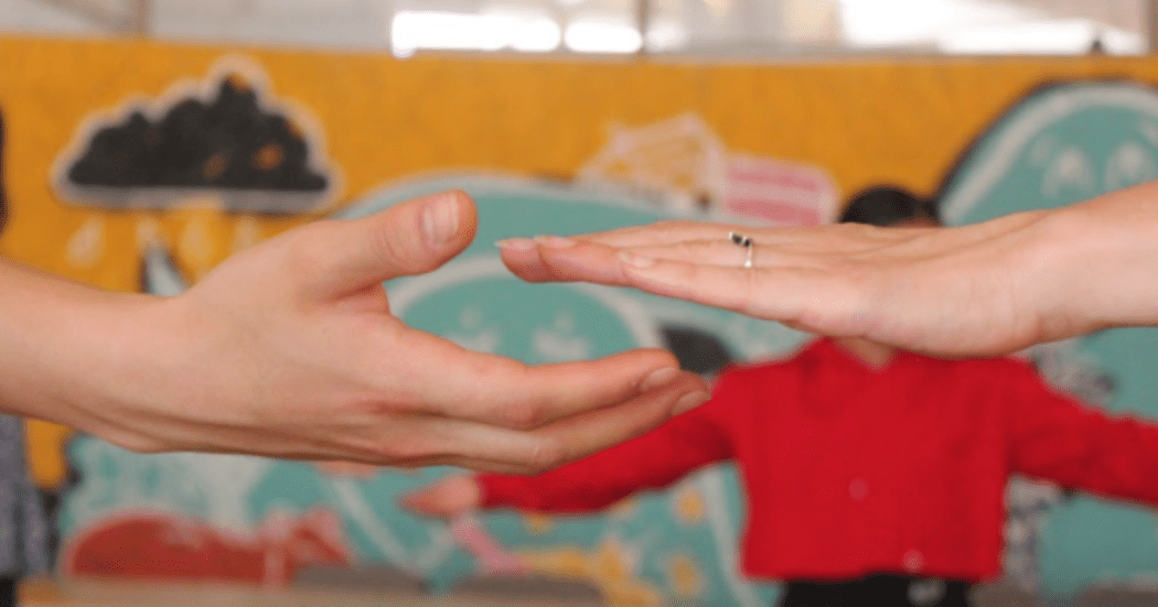 Imagen de dos manos que tratan de juntarse, de fondo se ve un hombre extendiendo la mano a su pareja de baile