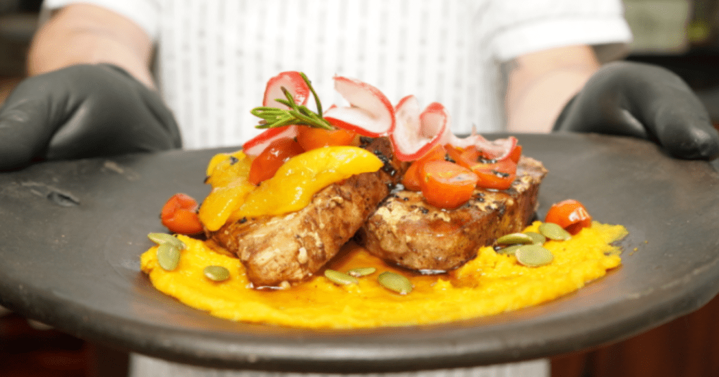 Imagen de una persona que tiene en sus manos un plato de una carne emplatada de manera típica.