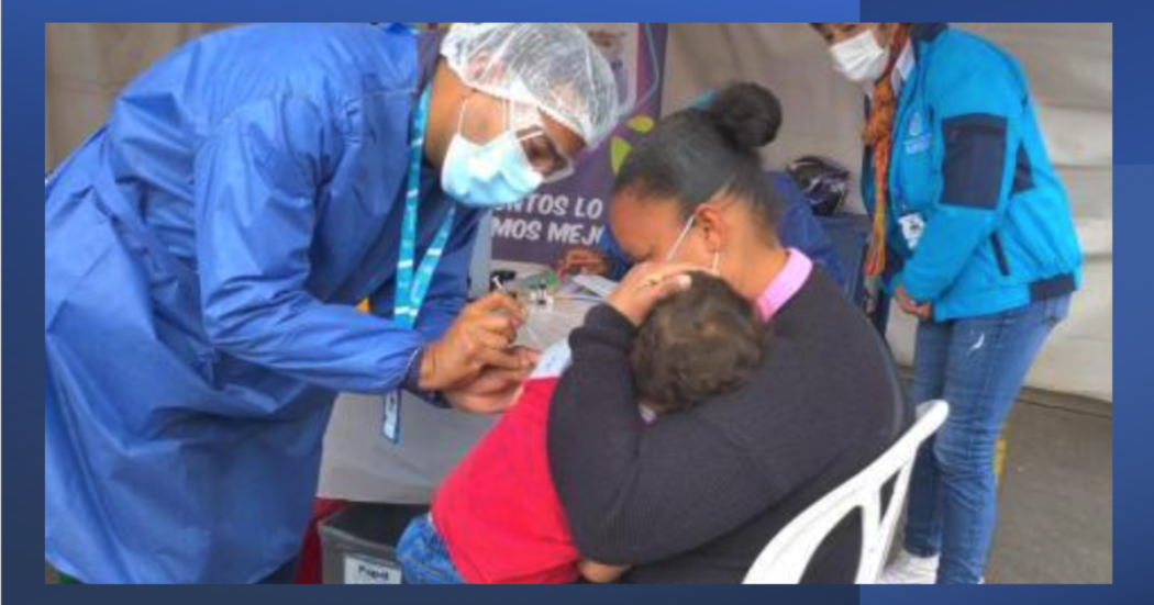 Imagen de una enfermara vacunando a un niño mintras su mamá lo carga en sus brazos.