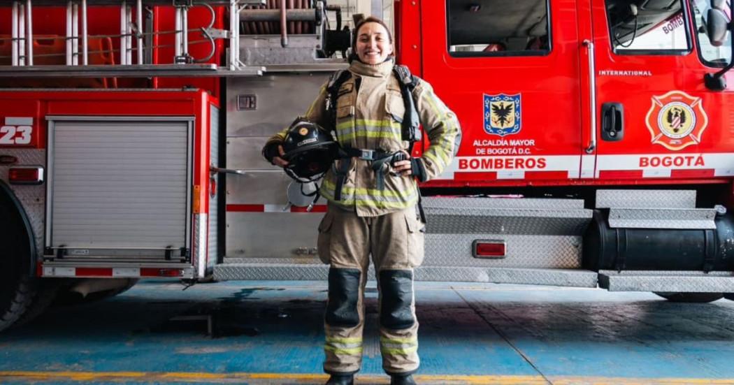 Mujer Bombera frente a un camión de bomberos.