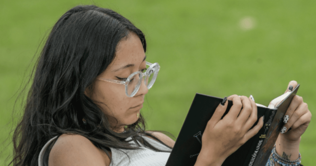 Imagen de una mujer leyendo un libro, sentada comodamente en un parque.