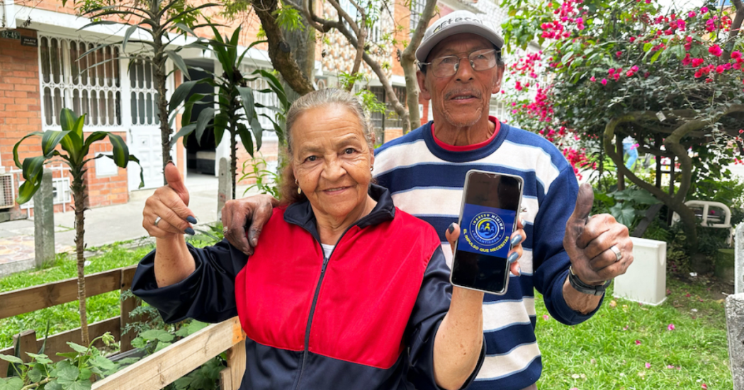 Imagen de dos personas mayores sonriendo y mostrando un celular con la imagen de Ingreso Mínimo Garantizado