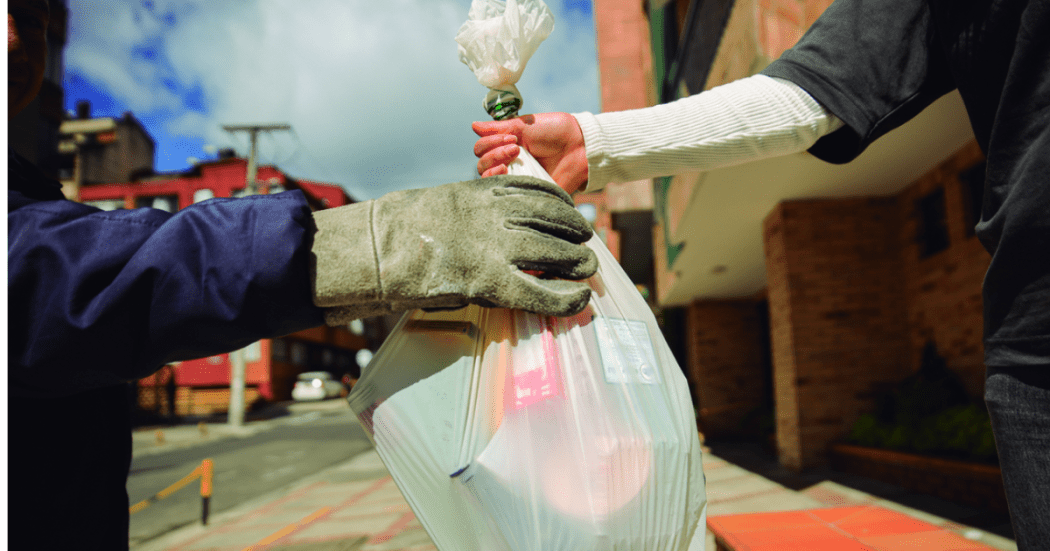 Imagen de una persona entregando una bolsa de basura a un recolector.