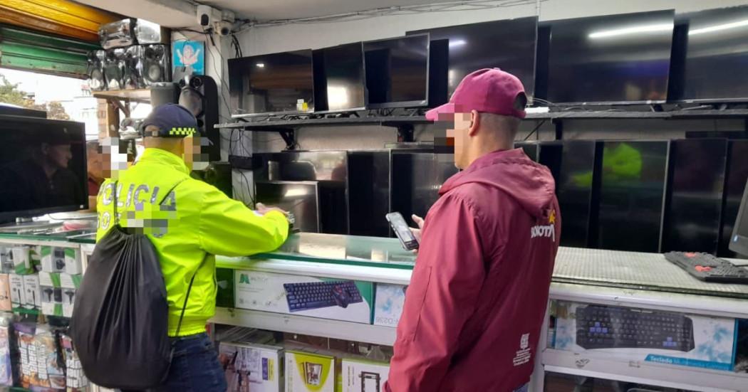 Policía y funcionario del Distrito inspeccionando establecimiento comercial dedicado a la compra y venta de equipos tecnológicos.