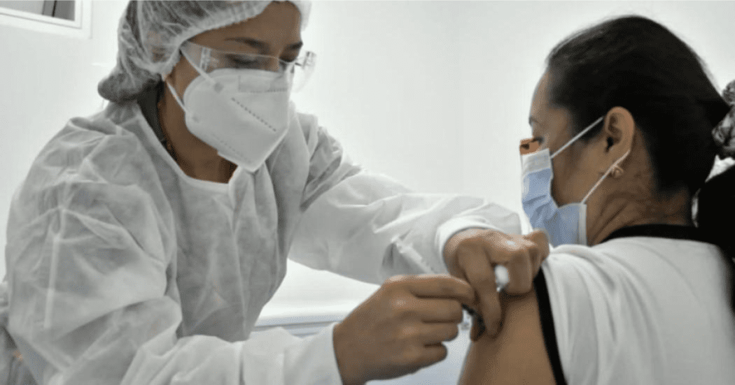 Imagen de una enfermera aplicando una vacuna a una mujer de mediana edad que usa tapabocas
