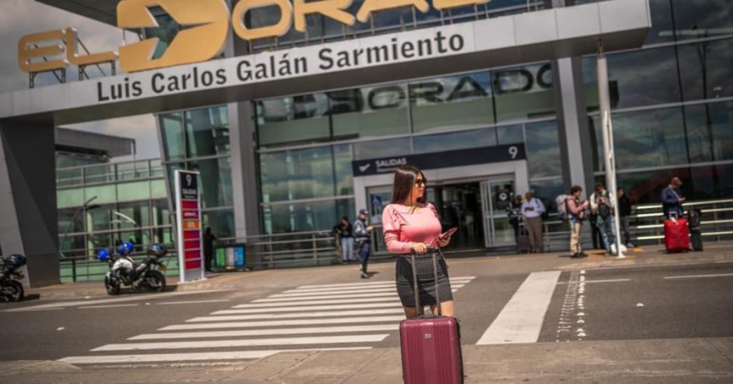 Foto de una mujer con su maleta de viaje frente al Aeropuerto Internacional El Dorado de Bogotá.