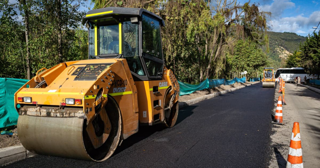 Maquina amarilla en operación pavimenta vía urbana con señalización vial 