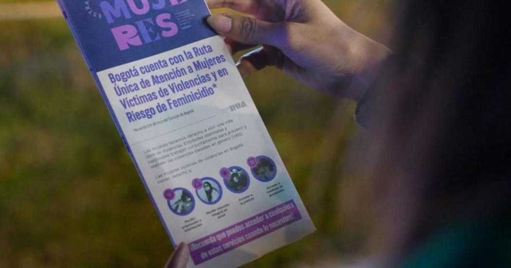 Mano sosteniendo folleto de la SDMujer en el que se lee: "Bogotá cuenta con la Ruta Única de Atención a Mujeres Víctimas de Violencias y en Riesgo de Feminicidio".