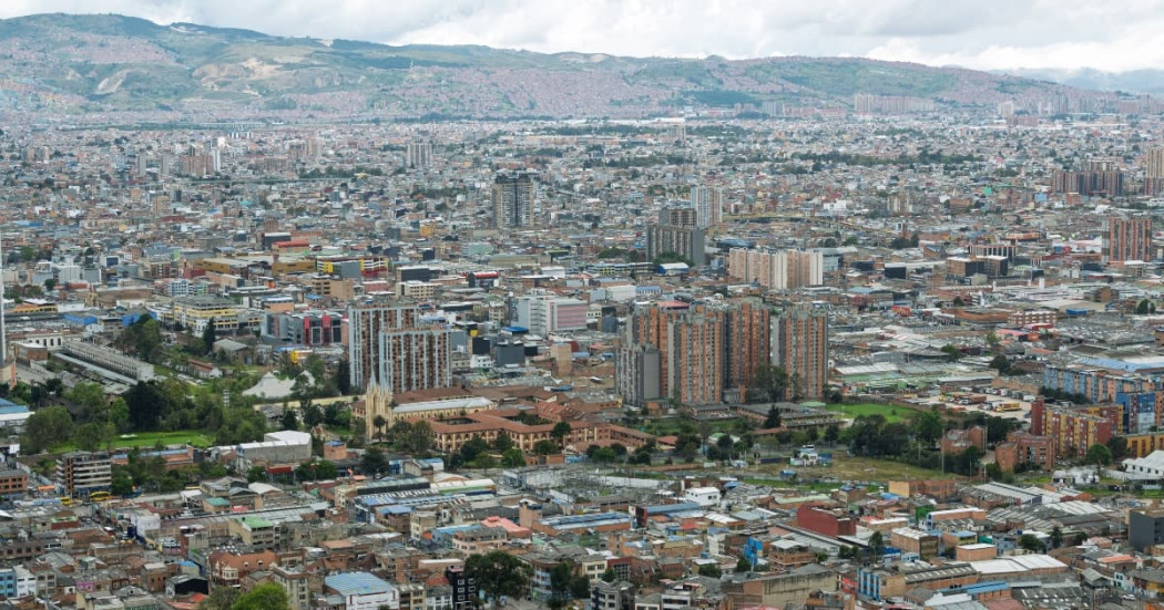 Panorámica de Bogotá con amplia zona urbana, edificaciones densas y cerros al fondo bajo cielo nublado