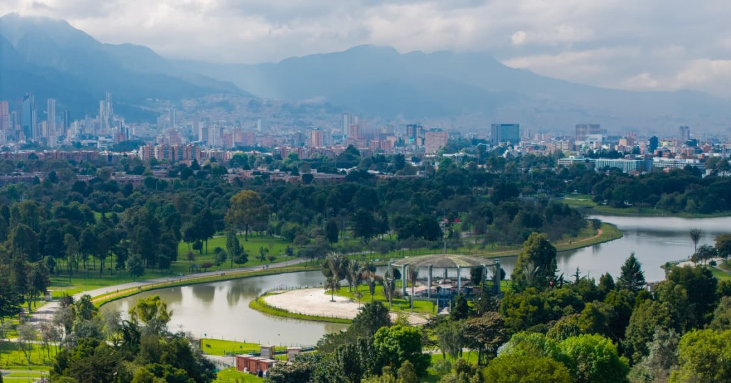 Vista panorámica de Bogotá, lago, senderos y arbolados de la ciudad con vista a montañas y cielo nublado
