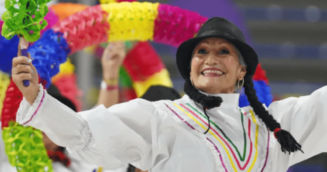Persona mayor participa en actividad cultural con vestuario tradicional y accesorios coloridos durante presentación recreativa