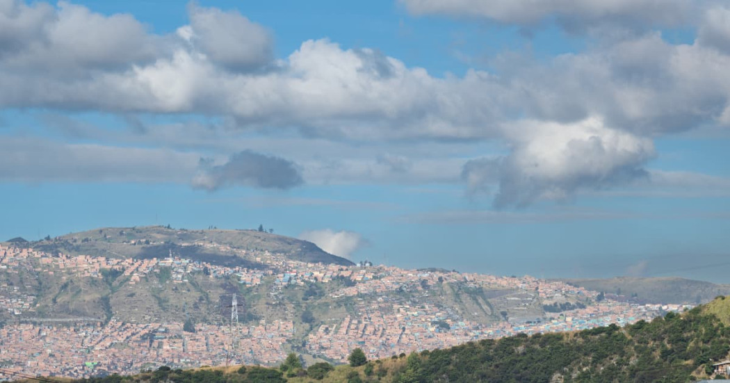 Panorámica de Bogotá con cerros poblados y cielo parcialmente nublado al fondo