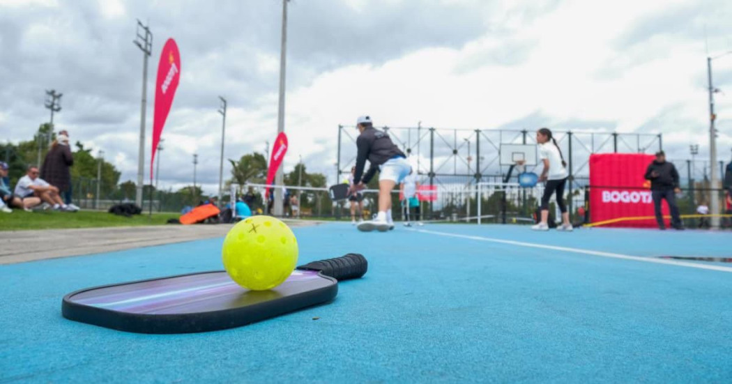 Raqueta de pickleball y una bola verde en un cancha para practicar este deporte