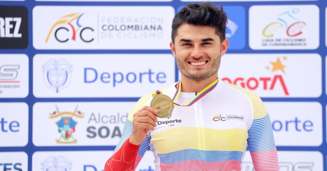 Edwin Matiz del Equipo Bogotá sostiene medalla dorada frente a panel institucional deportivo oficial nacional ciclismo