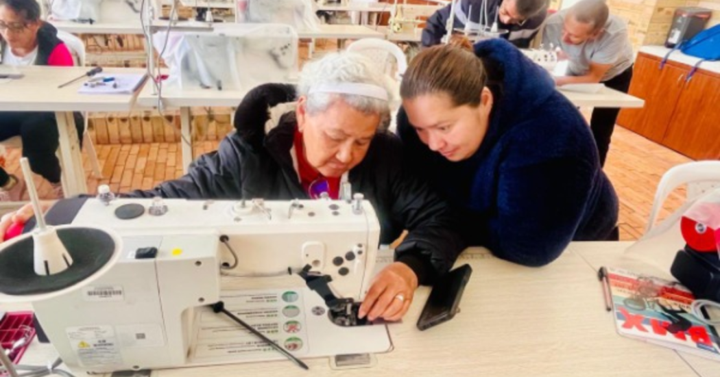 Imagen de una adulta mayor acompañada de una señora cosiendo