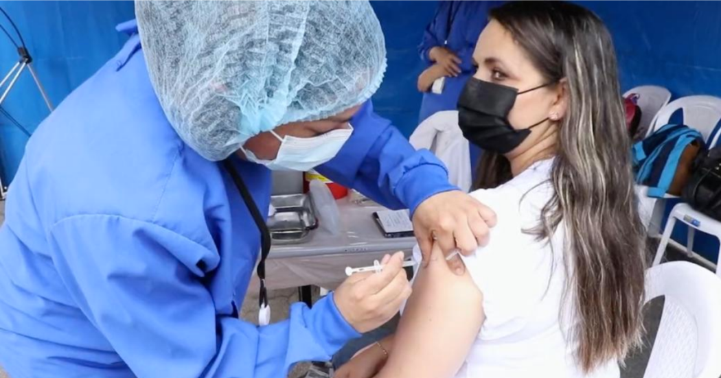 Imagen de una enfermera aplicando una vacuna a una mujer de mediana edad que usa tapabocas