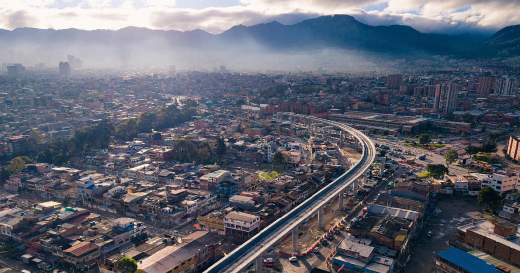 Panorámica aérea de Bogotá con trazado urbano, corredor vial elevado y cerros al fondo bajo neblina