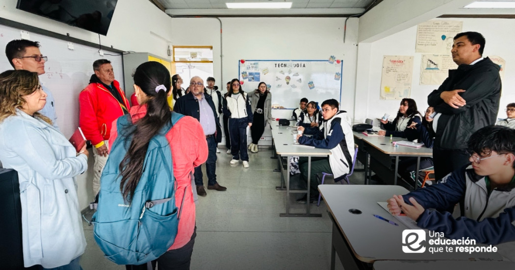 Foto que muestra un grupo de personas hablando dentro de un salón de clases