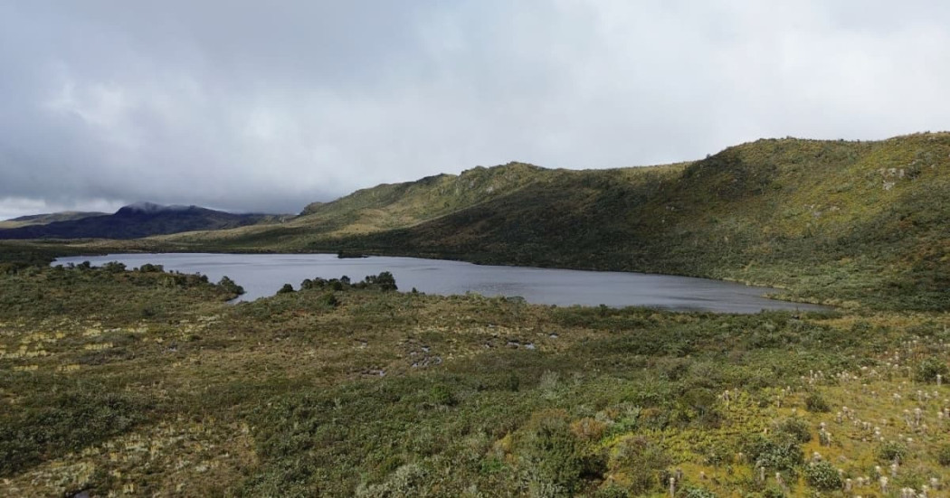 Laguna rodeada de vegetación natural y montañas bajo cielo nublado amplio