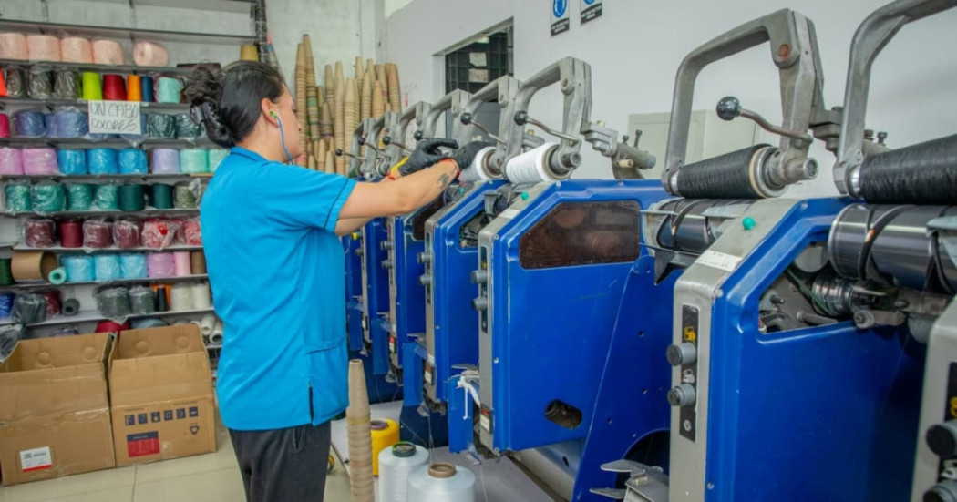Foto de una mujer trabajando junto a una maquina en una empresa de textiles en Bogotá.