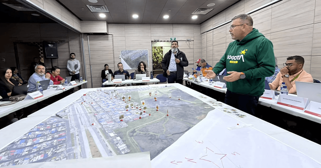 Autoridades distritales participan en simulación de manejo de emergencias alrededor de una mesa con mapas a gran escala, fichas de ubicación y material de planificación.