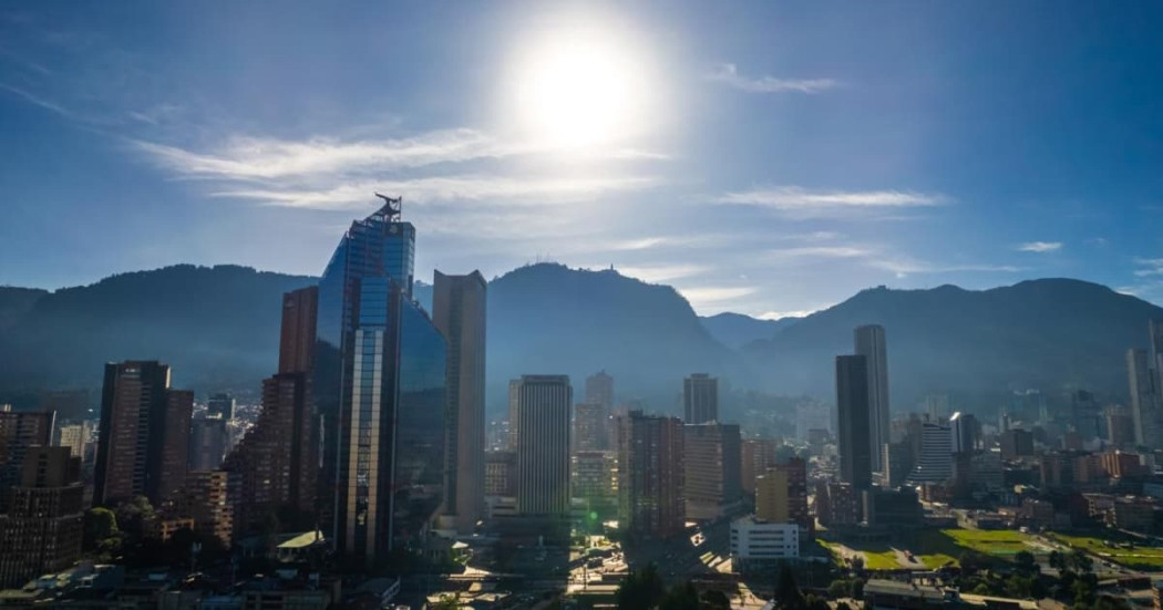 Vista panorámica de Bogotá con edificios modernos, cerros orientales y sol alto sobre cielo despejado