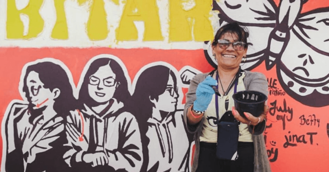 Mujer sonriente frente a un mural que ayudó a pintar.