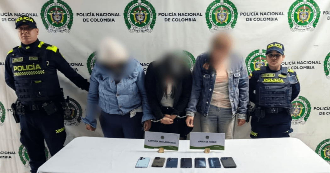 Tres mujeres capturadas en medio de dos policías. Los celulares recuperados están frente a ellas sobre una mesa.
