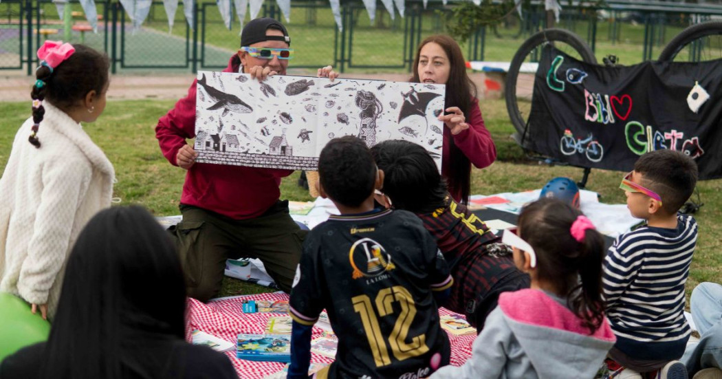 Imagen de dos personas mostranto un libro ilustrativo a niños en zona verde