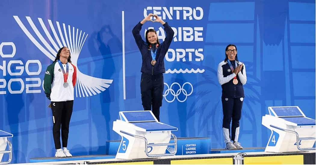 Deportistas reciben medallas durante ceremonia de premiación de los Juegos Centroamericanos y del Caribe Santo Domingo 2026, sobre el podio frente al panel oficial del evento.