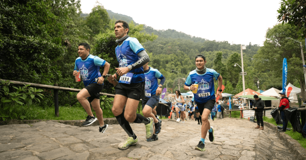 Participantes corren por el sendero empedrado de Monserrate rodeados de vegetación y público asistente.