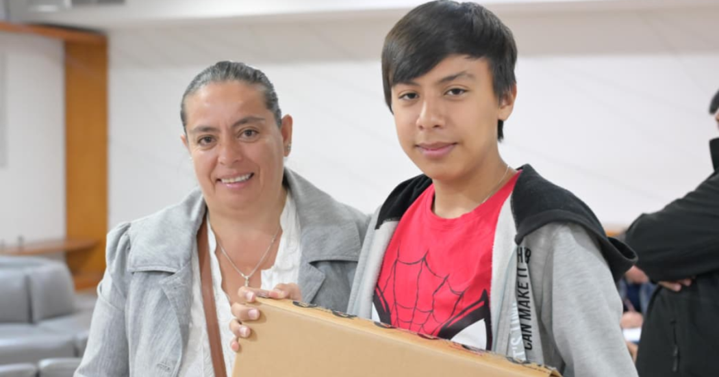 Imagen de Yasmín sonriendo junto a su hijo quien carga el computador