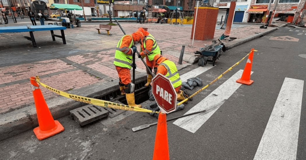 Foto que muestra dos personas con uniforme de Aguas Bogotá limpiando un sumidero