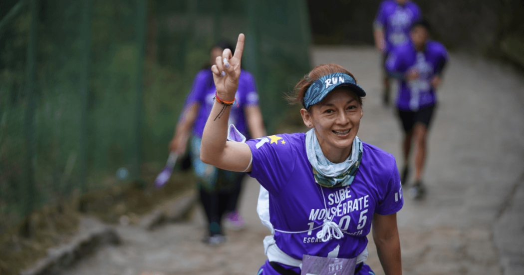 Imagen de referencia sobre participante de la carrera Sube Monserrate avanza por el sendero empedrado, viste camiseta morada con el texto “Sube Monserrate” y lleva el número de competencia sujeto a la cintura.
