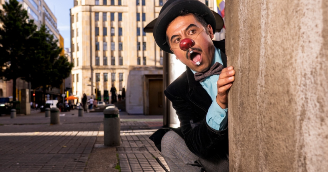 Imagen de Hombre con sombrero y nariz de payaso con corbatín asomándose por una columna de pared del Centro de Bogotá 