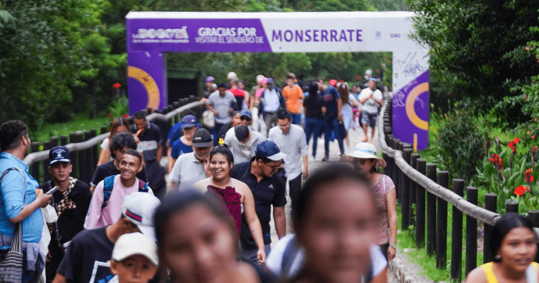 Visitantes recorren el sendero de Monserrate en Bogotá entre zonas verdes y barandas de madera, junto a un pórtico con el texto: “Gracias por visitar el sendero de Monserrate”.