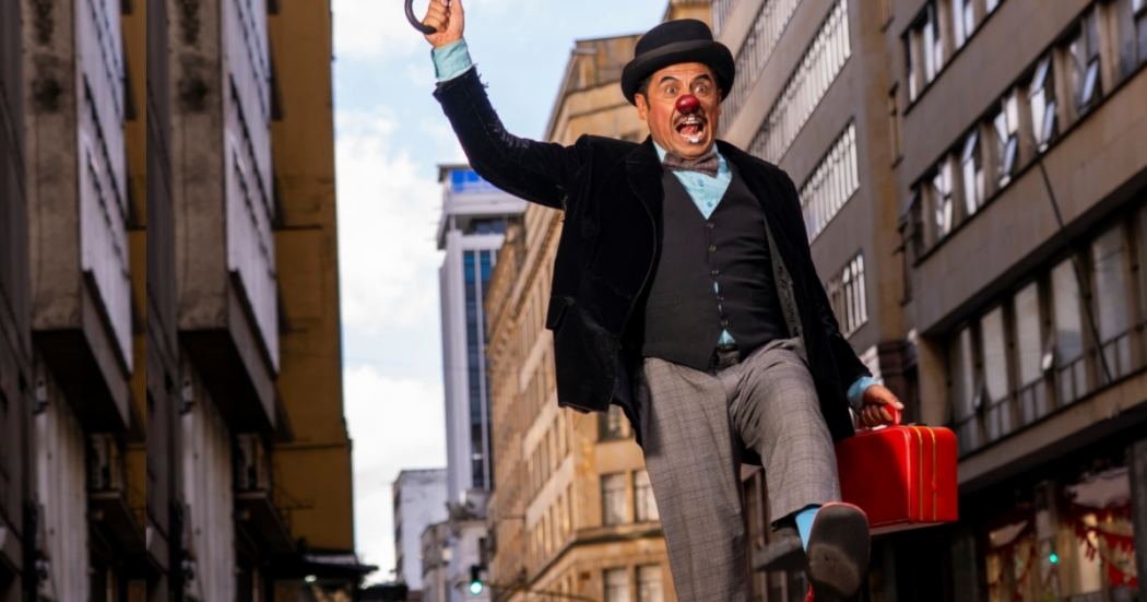 Imagen de un payaso que salta, al fondo se ven varios edificios grises y beige.
