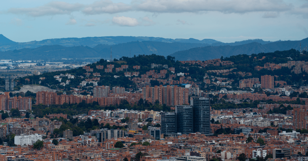 Vista panorámica de Bogotá con edificios residenciales y comerciales, cerros orientales y cielo nublado.