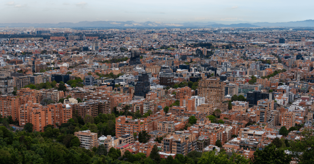 Vista panorámica de Bogotá con edificios residenciales y comerciales de mediana altura, zonas arboladas en primer plano y extensa expansión urbana hacia el horizonte.