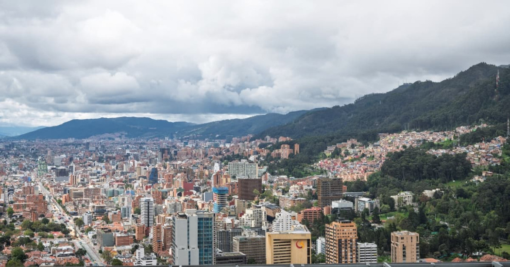 Vista panorámica de Bogotá con edificaciones densas, cerros orientales y cielo nublado amplio