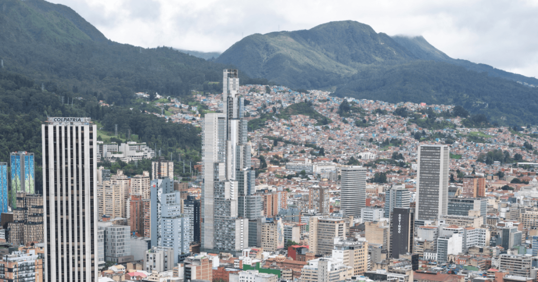 Vista panorámica del centro de Bogotá con edificios residenciales y empresariales de gran altura, cerros orientales cubiertos de vegetación y cielo nublado sobre la ciudad.