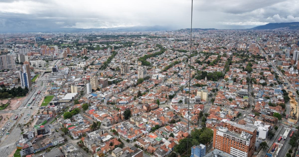 Vista aérea de Bogotá con amplia zona residencial, avenidas principales y numerosos edificios de baja y mediana altura, bajo cielo nublado con cerros visibles al fondo