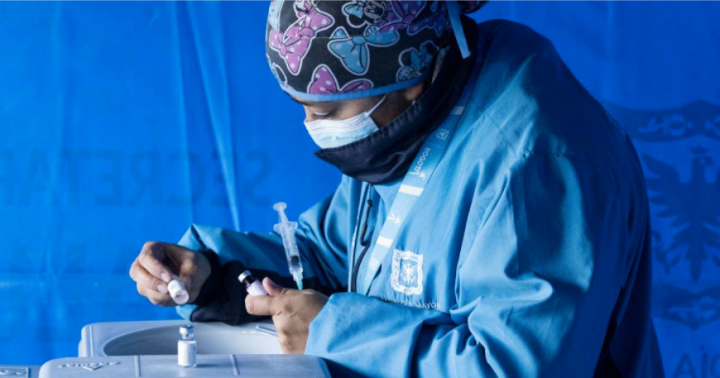 Imagen de una mujer vestida con chaqueta azul de la Secretaría de Salud preparando una geringa para vacunar.