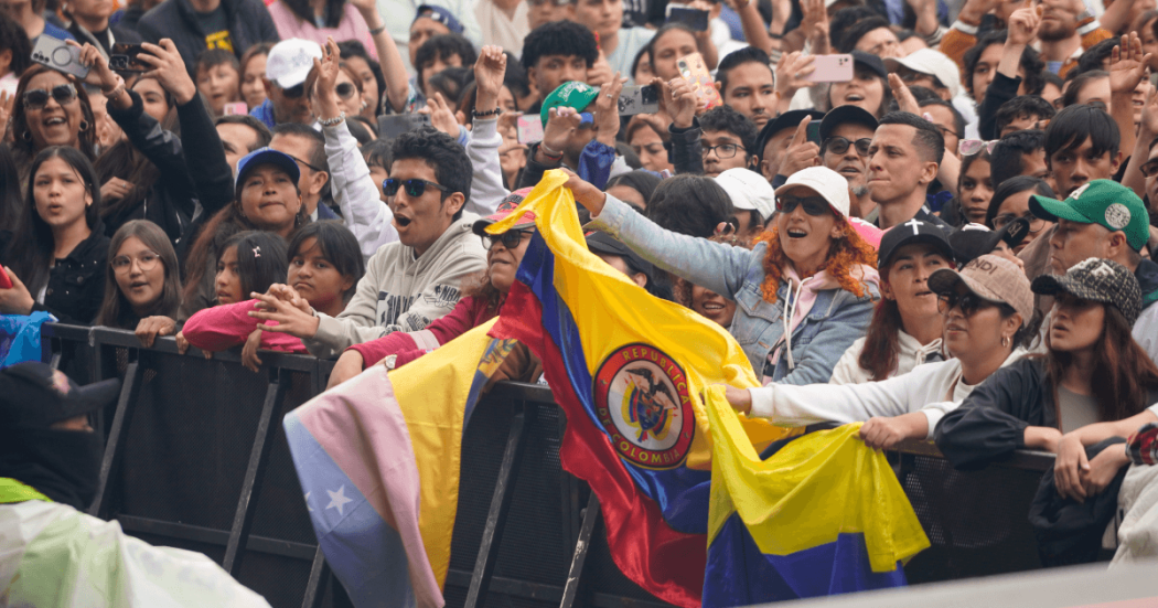 Asistentes a concierto en el parque Simón Bolívar permanecen frente a valla de seguridad del escenario, con banderas de Colombia visibles en primer plano.