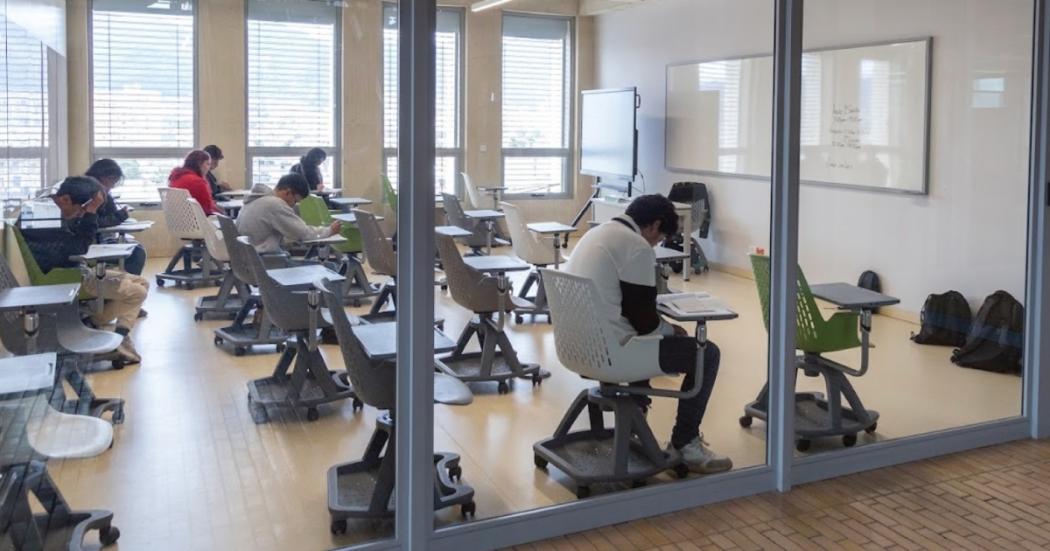 Foto que muestra estudiantes sentados en escritorios dentro de un salón